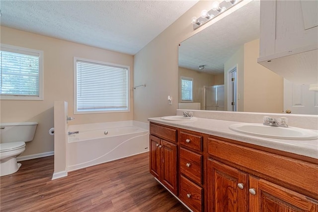 full bathroom featuring wood finished floors, a stall shower, double vanity, toilet, and a garden tub
