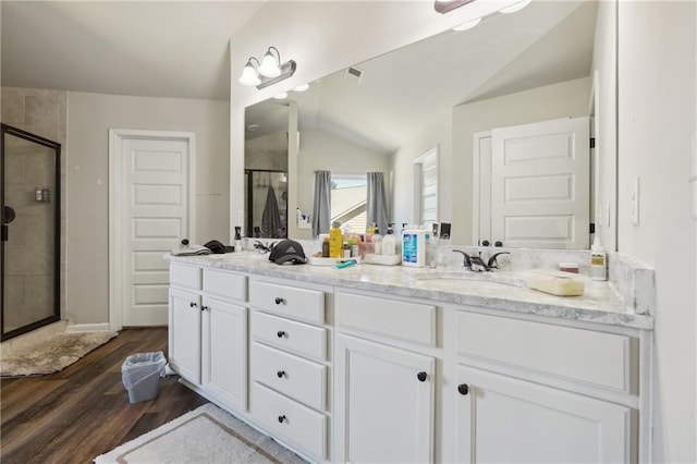 bathroom with lofted ceiling, wood finished floors, a sink, double vanity, and a stall shower