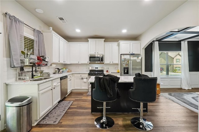 kitchen with arched walkways, visible vents, appliances with stainless steel finishes, white cabinetry, and a sink