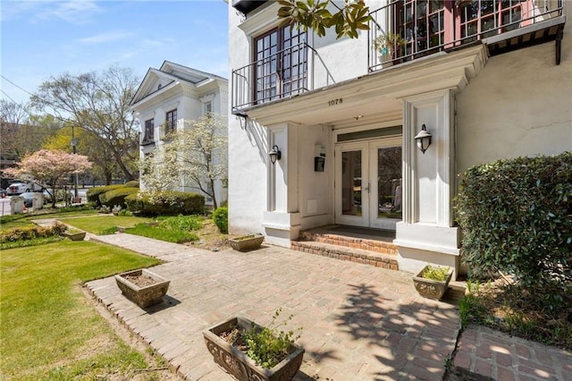 property entrance featuring french doors, a balcony, a lawn, and stucco siding