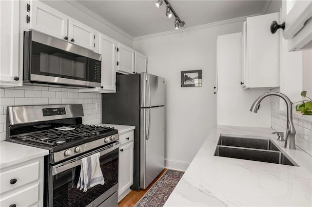 kitchen with appliances with stainless steel finishes, a sink, white cabinetry, ornamental molding, and rail lighting