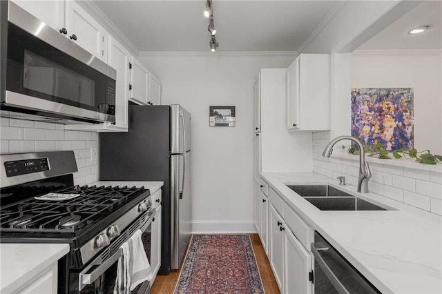 kitchen with stainless steel appliances, a sink, baseboards, white cabinets, and tasteful backsplash