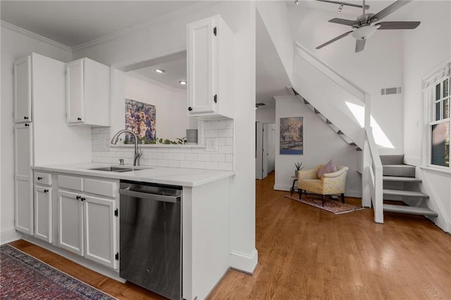 kitchen featuring stainless steel dishwasher, a sink, light countertops, light wood finished floors, and white cabinets