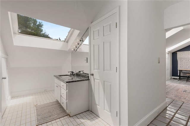bathroom with lofted ceiling, a skylight, tile patterned floors, vanity, and baseboards