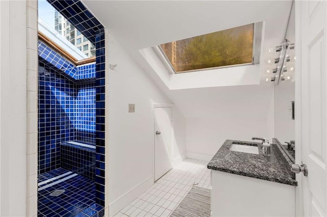 full bath featuring a skylight, tile patterned floors, a tile shower, vanity, and baseboards