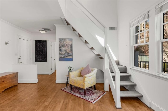 stairway with wood finished floors, ornamental molding, and baseboards
