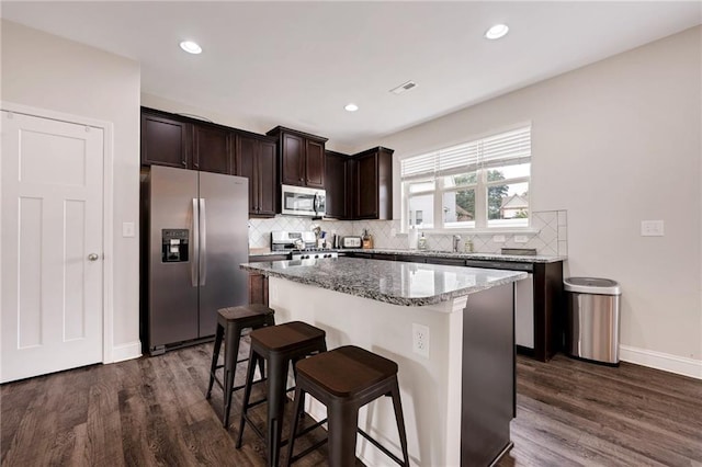 kitchen featuring stainless steel appliances, light stone counters, a center island, and dark hardwood / wood-style floors