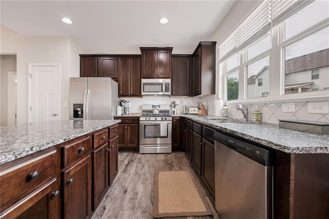 kitchen with appliances with stainless steel finishes, light hardwood / wood-style floors, backsplash, dark brown cabinets, and sink