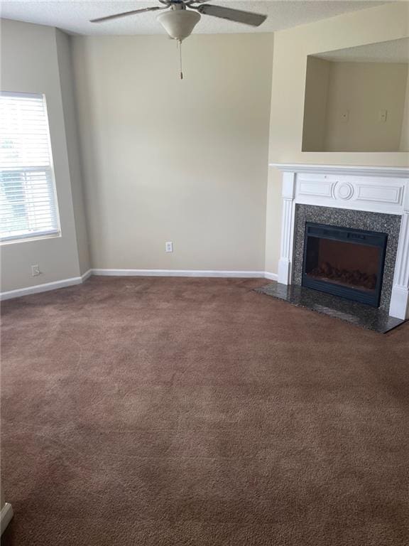 unfurnished living room featuring ceiling fan, dark carpet, a textured ceiling, and a fireplace