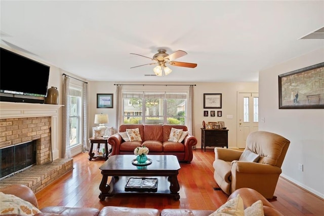 living room featuring ceiling fan, hardwood / wood-style floors, and a brick fireplace