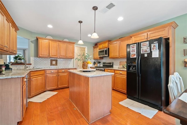 kitchen with pendant lighting, light hardwood / wood-style flooring, appliances with stainless steel finishes, a center island, and light stone counters