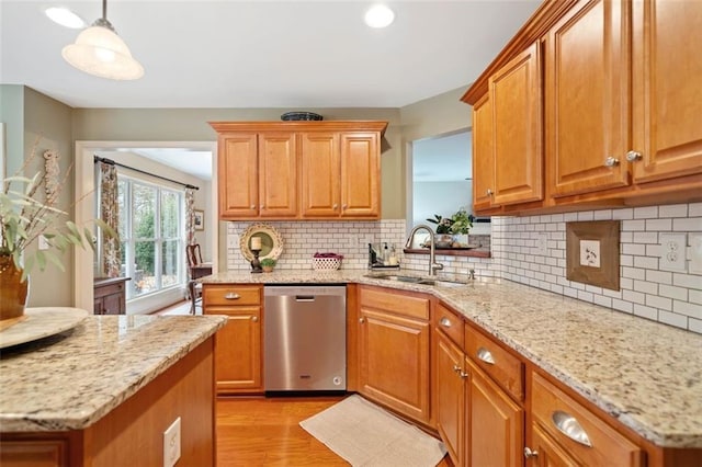 kitchen featuring sink, light hardwood / wood-style flooring, stainless steel dishwasher, pendant lighting, and light stone countertops