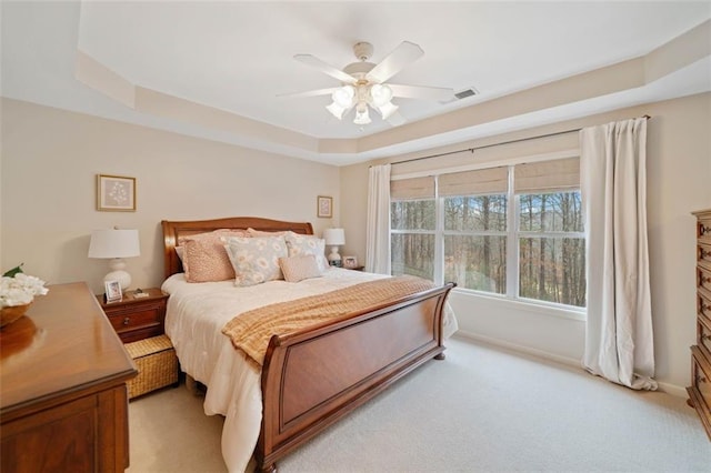 carpeted bedroom with ceiling fan and a tray ceiling