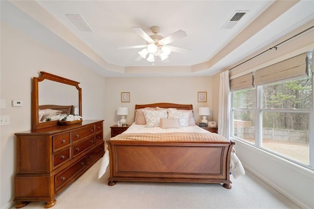 bedroom featuring ceiling fan, light colored carpet, and a tray ceiling