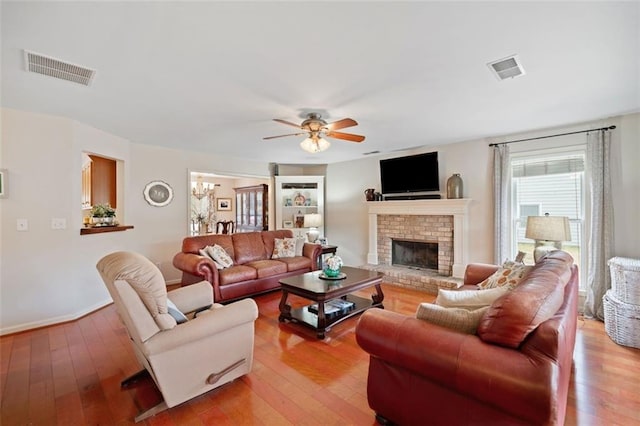 living room with a brick fireplace, ceiling fan, and light hardwood / wood-style flooring