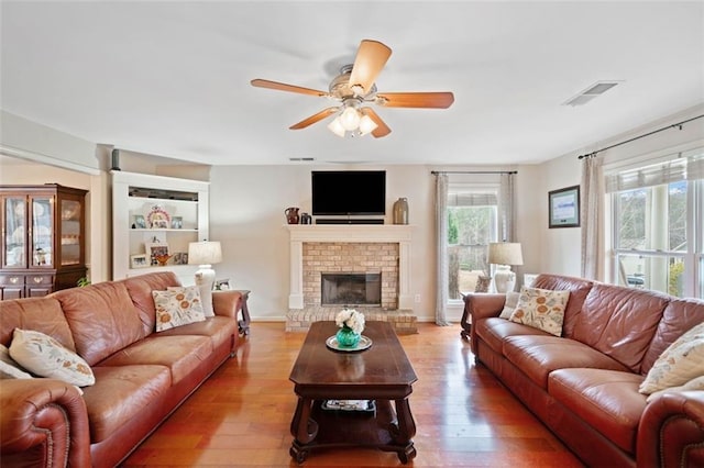 living room featuring ceiling fan, light hardwood / wood-style floors, and a brick fireplace