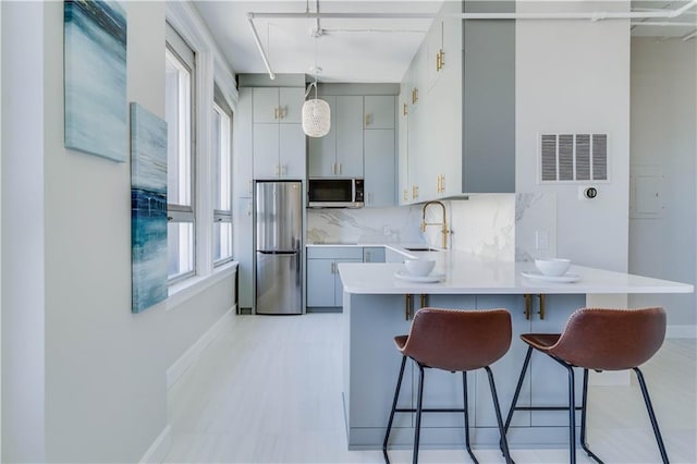 kitchen with a sink, appliances with stainless steel finishes, a breakfast bar, light countertops, and a peninsula