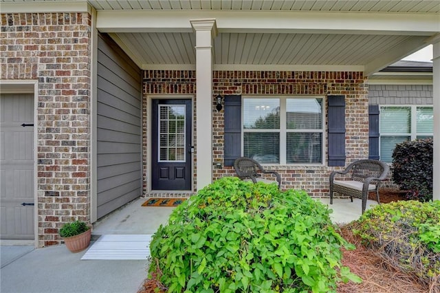 entrance to property featuring covered porch, brick siding, and a garage