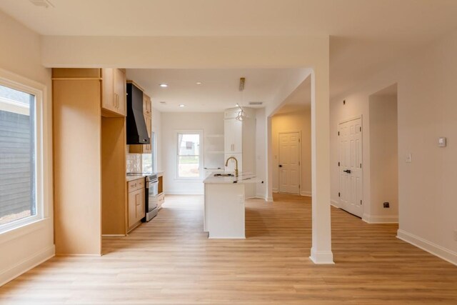 kitchen featuring electric stove, sink, wall chimney exhaust hood, and light wood-type flooring