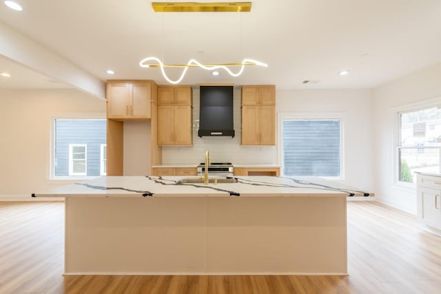 kitchen featuring a kitchen island with sink, hanging light fixtures, wall chimney exhaust hood, and light brown cabinets