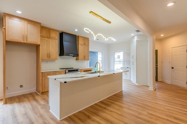 kitchen featuring wall chimney exhaust hood, sink, hanging light fixtures, electric range, and a kitchen island with sink