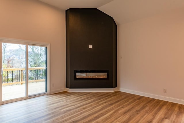 empty room featuring vaulted ceiling, a large fireplace, and light wood-type flooring