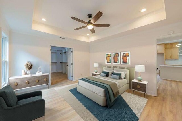 bedroom with ceiling fan, a tray ceiling, light hardwood / wood-style floors, and a spacious closet