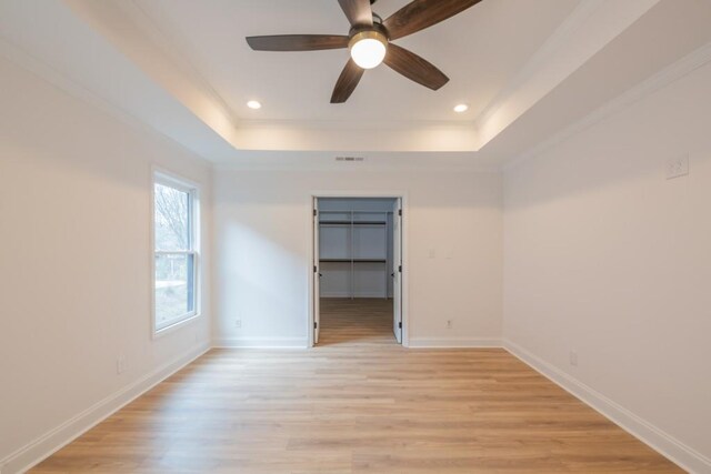 unfurnished room with ceiling fan, a raised ceiling, and light wood-type flooring