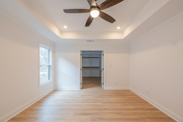 empty room featuring a raised ceiling, ceiling fan, and light hardwood / wood-style floors