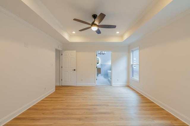 empty room with a raised ceiling, ceiling fan, and light hardwood / wood-style flooring