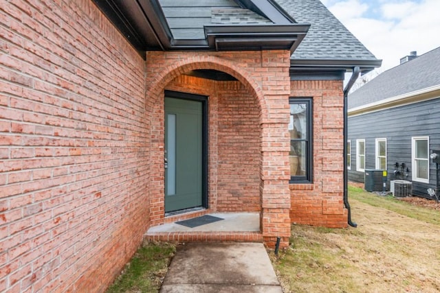 view of exterior entry with central AC and a lawn