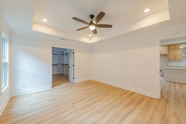 empty room with light hardwood / wood-style flooring, ceiling fan, and a tray ceiling