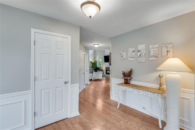 hallway with light wood-type flooring, a textured ceiling, and a wainscoted wall