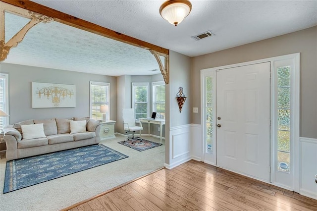 foyer entrance featuring wood-type flooring, wainscoting, and a textured ceiling