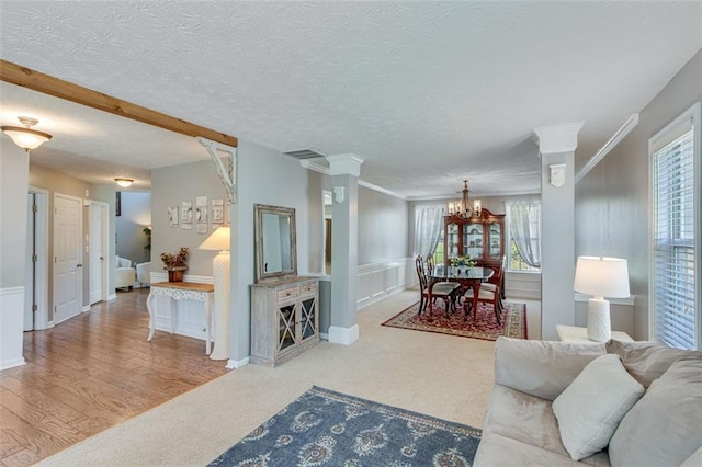living room featuring a chandelier, carpet flooring, crown molding, a textured ceiling, and a wainscoted wall