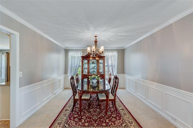 dining space with a chandelier, a decorative wall, light colored carpet, wainscoting, and crown molding