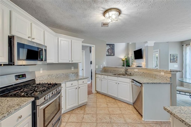 kitchen with stainless steel appliances, a sink, white cabinets, light stone countertops, and a peninsula