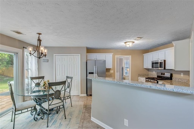 kitchen with stainless steel appliances, white cabinetry, light stone counters, and a textured ceiling