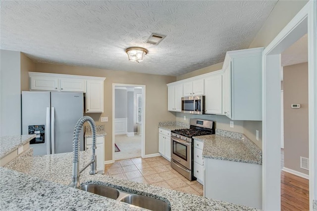 kitchen with stainless steel appliances, a sink, light stone counters, white cabinets, and baseboards