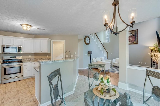 kitchen with stainless steel appliances, white cabinets, light tile patterned flooring, light stone countertops, and a textured ceiling