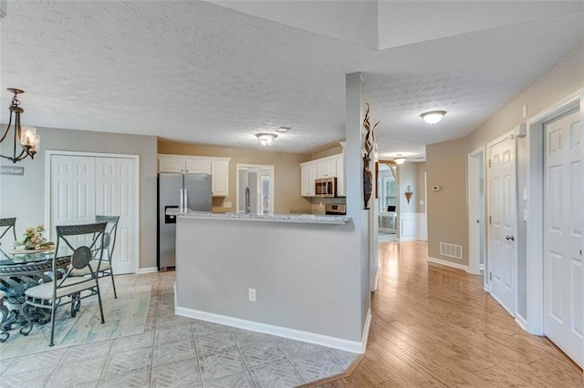 kitchen featuring stainless steel appliances, white cabinetry, a peninsula, baseboards, and light wood-type flooring