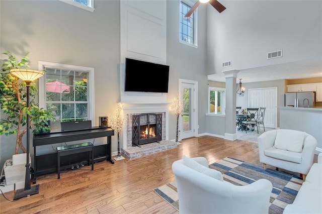 living area with a towering ceiling, light wood-style flooring, a fireplace, a ceiling fan, and baseboards