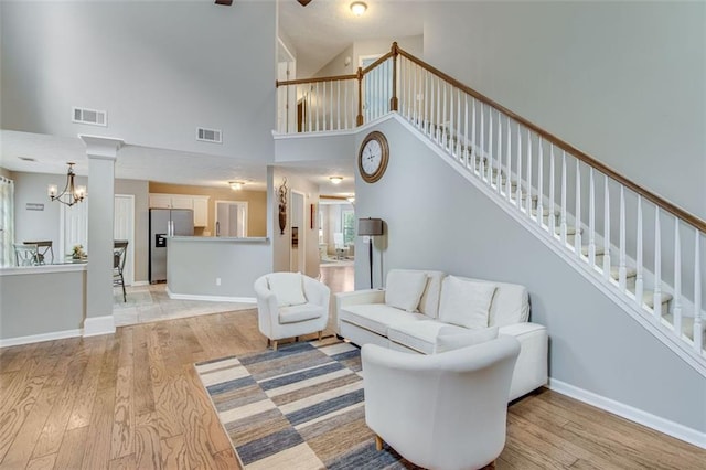 living area featuring light wood-type flooring, a chandelier, stairway, a high ceiling, and baseboards