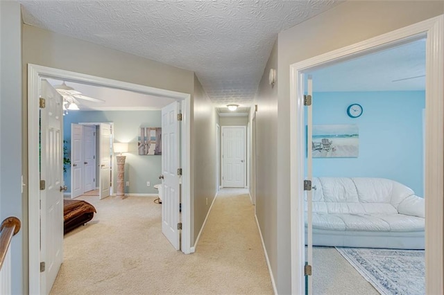 hall with light carpet, baseboards, and a textured ceiling