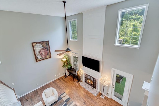 living area featuring a brick fireplace, wood finished floors, baseboards, and a ceiling fan