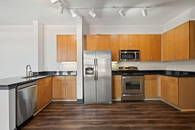 kitchen with dark wood finished floors, stainless steel appliances, dark countertops, a sink, and a peninsula