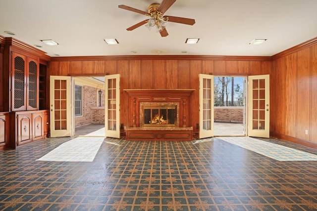 unfurnished living room featuring a glass covered fireplace, french doors, and wood walls