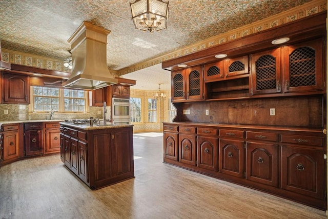 kitchen featuring wallpapered walls, light wood-style flooring, a notable chandelier, and a kitchen island with sink