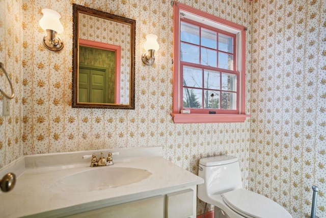 bathroom featuring toilet, wallpapered walls, and vanity