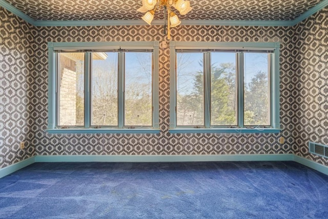 empty room featuring wallpapered walls, crown molding, baseboards, and dark colored carpet